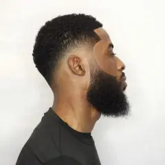 Hombre con barba tupida y corte de pelo con taper fade bajo, líneas definidas y degradado impecable.