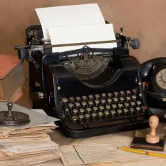 Escritorio antiguo con máquina de escribir, teléfono negro, libros y papeles. Un lápiz amarillo descansa sobre documentos, evocando la creación de dibujos con máquina de escribir.
