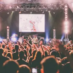 Koncert australijskiego zespołu rockowego. Tłum szaleje, ręce w górze, światła sceniczne.