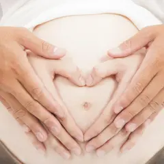 Dłonie tworzą serce na brzuchu w 4 miesiącu ciąży.