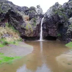 Cascada cayendo en el **charco de la paloma**, rodeado de rocas oscuras y vegetación.