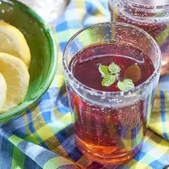 Un verre de jus de bissap pétillant, garni de menthe fraîche, à côté d'un bol de citrons tranchés. Parfait pour une journée ensoleillée.