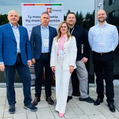 Pięć osób w eleganckich strojach stoi przed budynkiem, na tle banera z logo "m Finanse".
