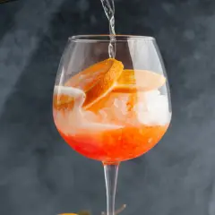 Orzeźwiający drink z cydrem, lodem i plasterkami pomarańczy, w trakcie nalewania.