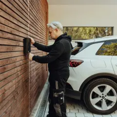 Un homme installe une borne de recharge pour voiture électrique sur un mur en bois. La question "peut on installer soi meme une borne de recharge" se pose.
