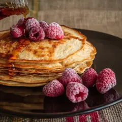 Pila de tortitas doradas con frambuesas congeladas y sirope cayendo. Una deliciosa receta de tortitas para disfrutar.