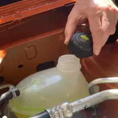 Mano quitando el tapón del depósito de anticongelante, que parece bajo. El anticongelante se evapora con el tiempo.