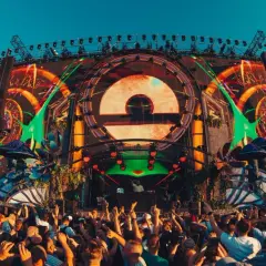 Tłum ludzi na festiwalu muzycznym przed wielką sceną z efektami świetlnymi i logo.