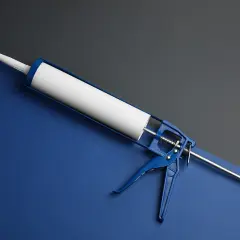 Niebieski pistolet do silikonu z białą tubą. Gotowy do pracy, gdy tylko pojawi się coś, co rozpuszcza silikon.