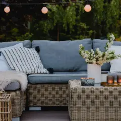 Przytulny duży taras w bloku aranżacje: wygodna szara sofa, wiklinowy stolik z latarenkami i świecami, wazon z kwiatami.