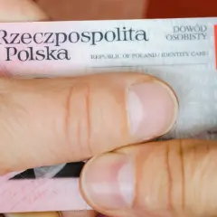 Dłonie trzymają polski dowód osobisty. Widoczna jest seria i numer dowodu, godło Polski oraz napisy "Rzeczpospolita Polska" i "Dowód osobisty".