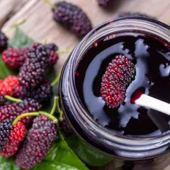 Un vasetto di marmellata di gelso frutto, con alcuni frutti freschi sparsi sul tavolo di legno.