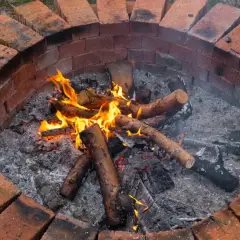 Płonące polana w okrągłym palenisku z cegły w ogrodzie.