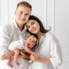 Szczęśliwa rodzina z noworodkiem w białych ubraniach, pozująca do sesji zdjęciowej.