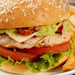 Pyszny burger z kurczakiem, z awokado, serem i chrupiącym bekonem, podany z frytkami.