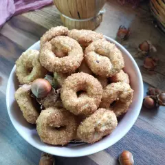 Ciambelline al vino ricetta originale, dorate e croccanti, con nocciole sullo sfondo.