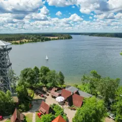 Wieża widokowa w **Kaszubskim Parku Krajobrazowym** nad jeziorem, z żaglówką na wodzie i zabudowaniami u podnóża.