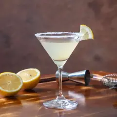 Elegancki martini bianco z solnym brzegiem i plasterkiem cytryny, obok połówki cytryny i oliwek.
