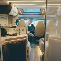 Wnętrze kampera, gotowego na podróż do Czarnogóry. Uśmiechnięty mężczyzna i pies czekają na przygodę.