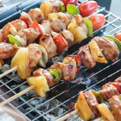 Na grillu piecze się kilka szaszłyków z kurczakiem, ananasem, papryką i pomidorkami.