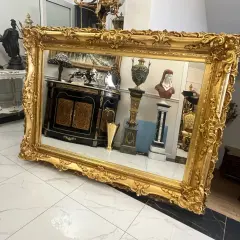 Wspaniałe lustro w bogatej, złotej ramie, odbijające antyczne meble i dekoracje.