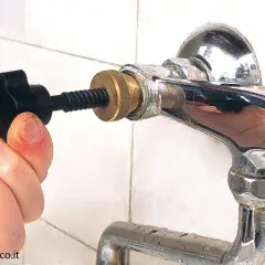Strumento per sbloccare un rubinetto bloccato dal calcare. La mano stringe la manopola nera per agire sul meccanismo.