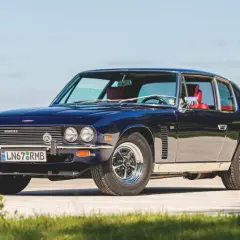 Mörkblå Jensen Interceptor med röda säten, parkerad utomhus på en solig dag.