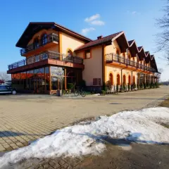 Pomarańczowy budynek z balkonami i przeszklonym parterem, stojący przy drodze nad jeziorem. Roś.