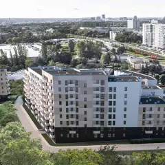 Nowoczesne bloki mieszkalne otoczone zielenią, w tle miejski krajobraz Poznania.