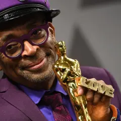 Spike Lee, w fioletowym garniturze i czapce, trzyma Oscara z napisem "LOVE". Jego filmy często poruszają ważne tematy społeczne.