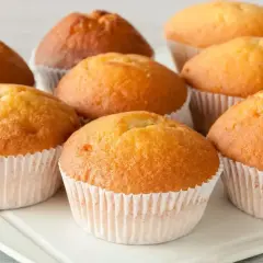 Kilka puszystych, złotobrązowych muffinek w papierowych foremkach na białej tacy.