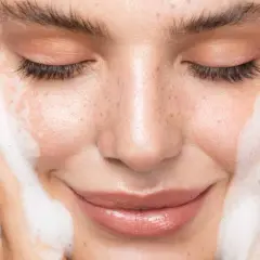 Une femme se nettoie le visage avec de la mousse. Un geste simple pour un teint frais, découvrez comment nettoyer son visage pour une peau éclatante.