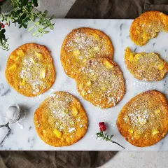 Saffranscookies med vit choklad, pudrade med florsocker, ligger på ett marmorfat. En bit är tagen från en cookie.