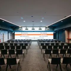 Moderne Konferenzräume im Kulturhaus Arena, bereit für Ihr Event. Reihenweise Stühle und eine große Leinwand mit der Botschaft "Wir machen Ihr Event zum Heimspiel!".