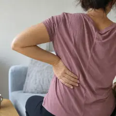 Donna con mano sulla schiena, soffre di mal di schiena e forse gastrite.