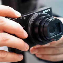 Dłonie trzymają aparat Sony RX100 VII z obiektywem Zeiss.