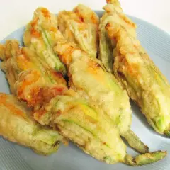 Fiori di zucca ripieni di ricotta, dorati e croccanti, serviti su un piatto azzurro.