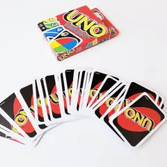 Karty do gry UNO rozłożone wachlarzem, obok pudełko. Poznaj zasady gry w UNO i zacznij zabawę!