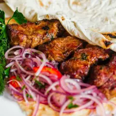 Soczyste mięso kebab zawinięte w placek, podane z czerwoną cebulą i świeżą natką pietruszki.