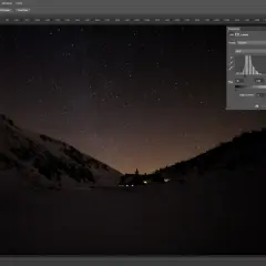 Nocne zdjęcie nieba nad ośnieżonymi górami, z widocznym domkiem i gwiazdami.