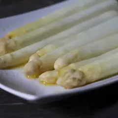 Zarte Spargelspitzen, perfekt gegart im Sous-Vide-Verfahren, liegen auf einer weißen Platte und glänzen in Butter.