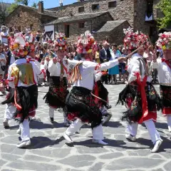 Hombres con trajes tradicionales y sombreros florales bailan en la plaza durante el **Día del Corpus**.
