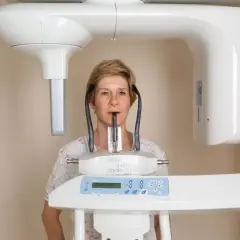 Kobieta poddaje się badaniu pantomograficznemu. Czy rentgen jest szkodliwy? Nowoczesne aparaty minimalizują ryzyko.
