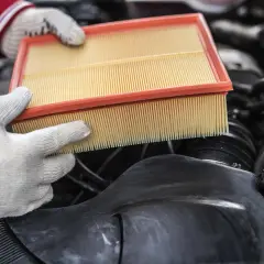 Mains gantées tenant un filtre à air propre, prêt à remplacer un filtre à air encrassé dans un moteur de voiture.
