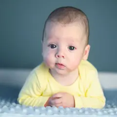 Uroczy niemowlak w żółtym body leży na niebieskim kocyku. Dziecko jest badane pod kątem retinopatii wcześniaczej.