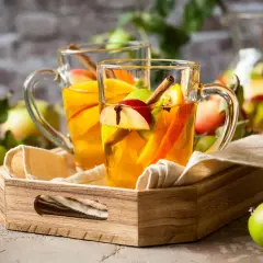 Zwei Gläser mit warmem Apfel-Zimt-Wasser, garniert mit Apfelstücken und Zimtstangen, stehen auf einem Holzteller.