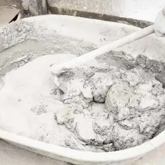 Mieszanie zaprawy z wapna gaszonego w dużej misie. Ręka w rękawicy miesza gęstą, szarą masę.
