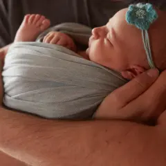 Otulony w miękkie pieluszki muslinowe noworodek śpi w ramionach taty.