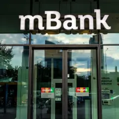 Logo mBank nad wejściem do placówki. Na drzwiach naklejki informujące o usługach, np. jak zablokować kartę mbank.