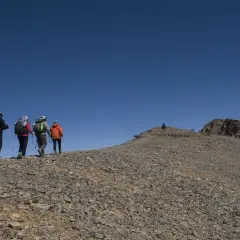 Randonneurs sur le flanc rocailleux du mont M'goun, sous un ciel bleu intense.